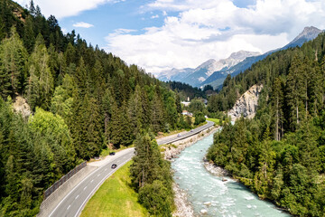 Scenic view of winding road beside a turquoise river surrounded by mountainous terrain and lush forests during day