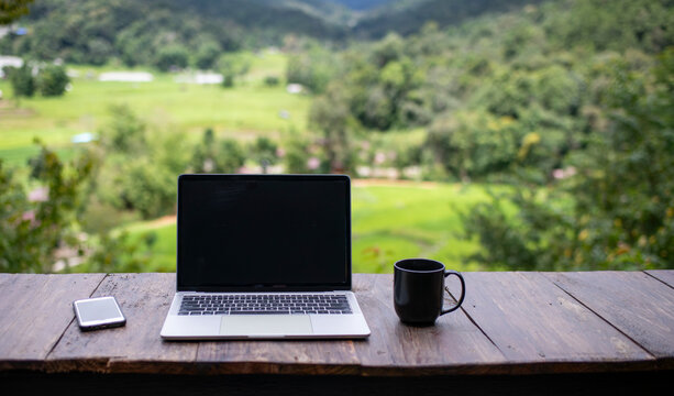 laptop computer on a wooden table with notebook in nature with a green mountain tropical background is work out side concept.