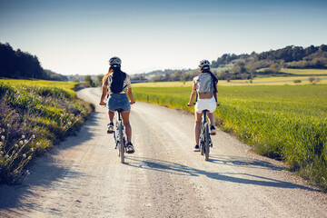 cheerful women friends cycling through rapessed field