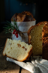Two homemade Christmas panettone , one cut and the other whole, with pine and red berries decorations on wooden table on rustic kitchen .