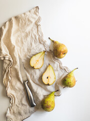 Whole pears and cut pears together with a cloth and a knife over a white counter