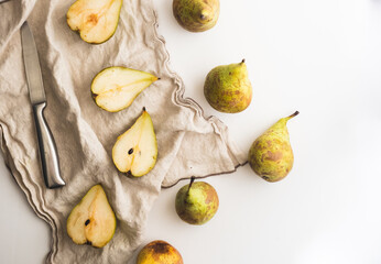 Whole pears and cut pears together with a cloth and a knife over a white counter
