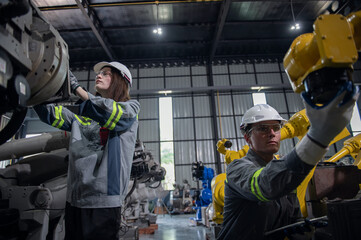 Engineer standing by robotic arm and operating machine in industry factory, technician worker check...