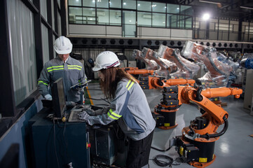 Engineer standing by robotic arm and operating machine in industry factory, technician worker check for repair maintenance electronic operation
