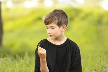 A young boy in a black shirt looks thoughtfully to the side while gently holding a blade of grass....