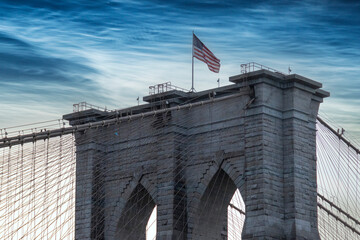Fototapeta premium Brooklyn Bridge spans the East River with clear blue skies and city skyline in the background during a bright sunny day in New York City