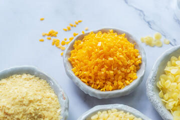 natural yellow beeswax pellets in white ceramic plate on white marble background.