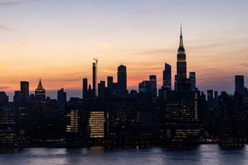 Fototapeta premium Stunning sunset over the New York City skyline highlighting iconic buildings and reflections on the water