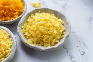 natural yellow beeswax pellets in white ceramic plate on white marble background.