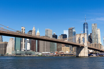Naklejka premium Brooklyn Bridge spans the East River with clear blue skies and city skyline in the background during a bright sunny day in New York City