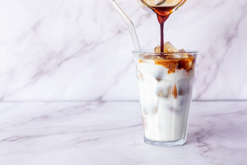 a glass of iced latte coffee with glass straw on white marble table background.