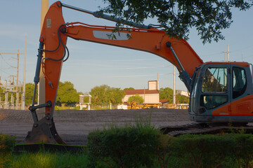 Wide framed view through orange bucket excavator machine at construction site of Electric Substation View over dirt pile with green grass in foreground.Electric poles with blue sky and white clouds.La