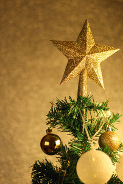 Close-up shot of a Christmas tree with a star on top, ornamented with yellow spheres and lights. Preparation for celebrate new year concept idea.