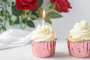 Pink cupcakes with tall buttercream swirl and a lit candle, cupcakes in pink foil liners with vanilla buttercream and a candle