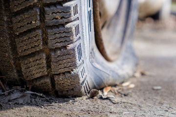 an old flat car tire. a puncture in a car tire. a hole in a tire and low tire pressure due to a puncture or long periods of standing without driving