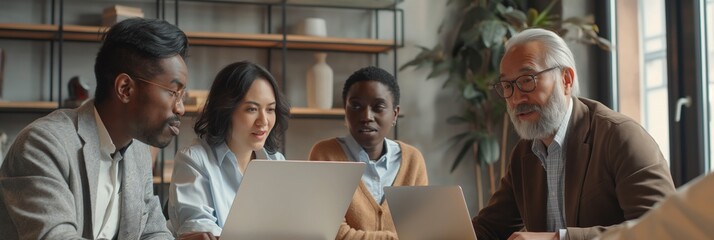A group of people are sitting around a table with laptops open, working together. Scene is collaborative and focused