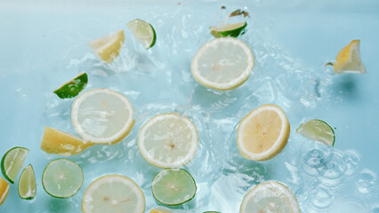 Macro of a sliced lemon dropping in to water with lemon and lime floating at blue background .Citrus fruit movement moving at clear water. Citrus freshness. Freshness and hydration concept. Pabulum.