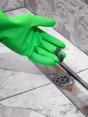 Clogged drain in the shower room. A gloved hand reveals debris and hair.