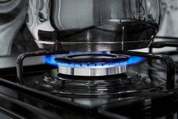Close-up of stainless steel pot on burner with blue flame on gas stove in home kitchen.