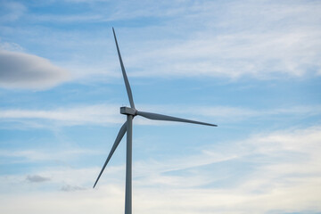 A wind turbine is standing tall in the sky, with a blue sky behind it