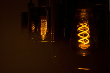 Glow from an incandescent lamp in complete darkness. The spiral lamp glows in a dark room. A modern...