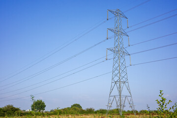 A electric high voltage transmission tower amidst open countryside under a clear blue sky.
