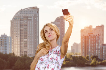 Mature blonde woman making a selfie on the frontal photo camera outdoors. Residential area...
