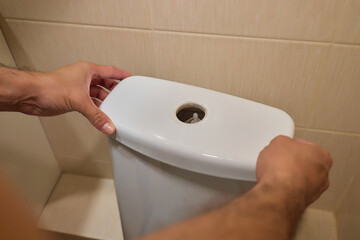 A Man Opening a Toilet Tank for the Purpose of Maintenance or Repair Tasks at Home