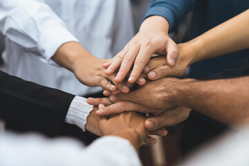 Obraz premium Group of diverse office worker join hand together in office room symbolize business synergy and strong productive teamwork in workplace. Cooperation and unity between business employee. Prudent