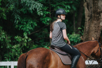 Young girl enjoying horseback riding on a brown horse outdoors, surrounded by lush greenery.