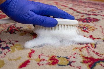 Hand with latex glove holding a white brush, on a natural fiber rug with white foam, abstract...