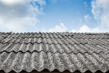 Gray asbestos sheets on a house rooof, pespective view with blue sky and white clouds © Dorin