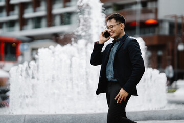 Urban Professional on the Go: Young businessman in a suit, engrossed in a phone call, strides...