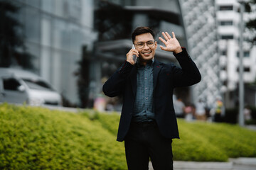 Confident Asian businessman waving and talking on the phone