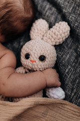 Sweet tiny newborn baby's hand hugging stuffed beige rabbit toy