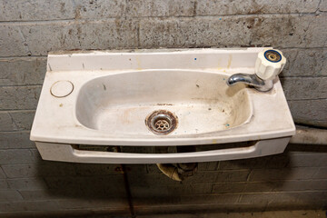 Photograph of an old and dirty wash basin in a factory bathroom.