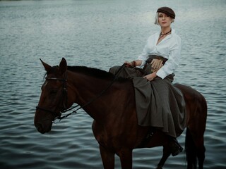 stylish blonde in white shirt dark skirt and cap with dark horse in dark blue water, cinematic...