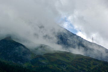 View of an amazing mountain landscape on a hazy day with gray clouds and fog over the peaks in autumn in Austria.