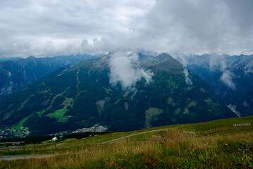 View of an amazing mountain landscape with a village in the valley on a hazy day with gray clouds and fog over the peaks in autumn in Austria.