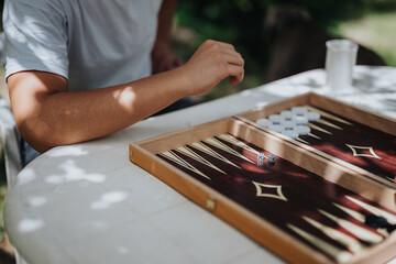 Person playing backgammon outside, enjoying a leisure activity on a sunny day. Hand about to make a...