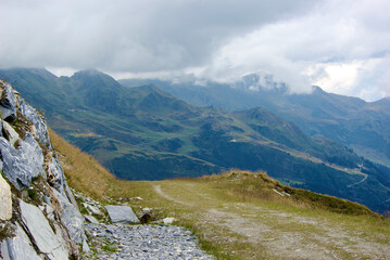 View of an amazing mountain landscape with a stony path on a hazy day with gray clouds and fog over the peaks in autumn in Austria.