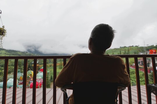 Asian woman sitting  back turned alone, looking lonely, admiring  mountain view with morning mist on balcony house, alone depressed looking seem so sadness lonely - Powered by Adobe
