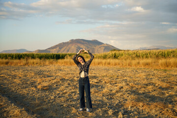 A Joyful Young Woman is Posing in a Scenic Golden Field Surrounded by a Beautiful Mountain View