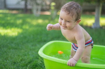 Cute baby boy bathes in a basin outdoors in summer.
