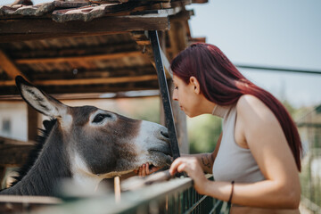 A young woman leans close to a donkey, showing a moment of connection and care at a rural farm...