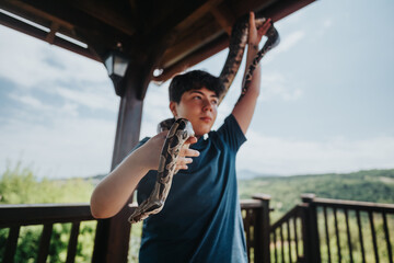 A young person holding and interacting with pet snakes outdoors on a sunny day, expressing joy and curiosity in a natural setting.