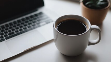 A cup of coffee sits on a desk next to a laptop