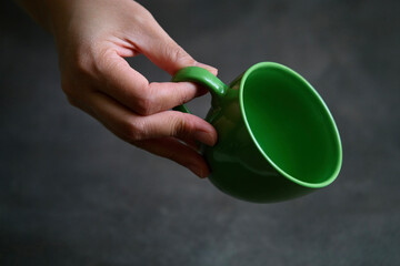 A woman’s hand holds a green coffee mug. Close-up 