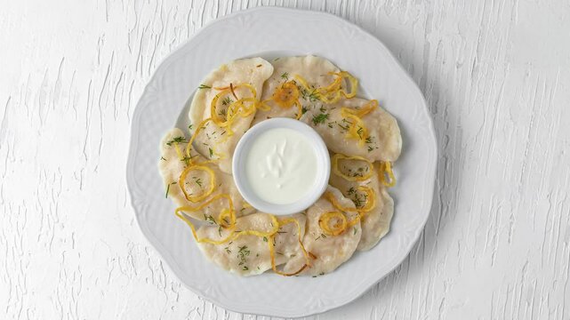 plate with dumplings, fried onions and sour cream rotating top view on white wooden background