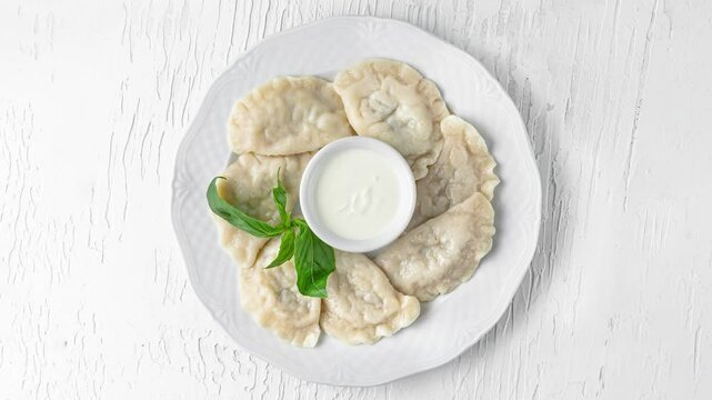 plate with dumplings, green spinach and sour cream rotating top view on white wooden background